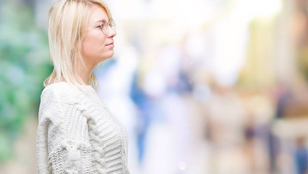 Mladá krásná blondýna žena nosí zimní svetr a brýle izolované pozadí pohledu na stranu, uvolnit profilu pozice s přirozenou tvář s sebejistý úsměv. - Fotografie, Obrázek