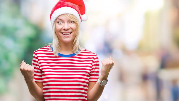 Jonge mooie blonde vrouw met kerst hoed over geïsoleerde achtergrond vieren verrast en verbaasd voor succes met armen aan de orde gesteld en ogen open. Winnaar concept. - Foto, afbeelding