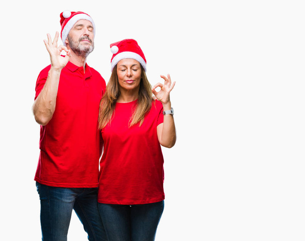 Латиноамериканская пара средних лет в рождественской шляпе на изолированном фоне расслабляется и улыбается с закрытыми глазами, делая жест медитации пальцами. Концепция йоги
. - Фото, изображение