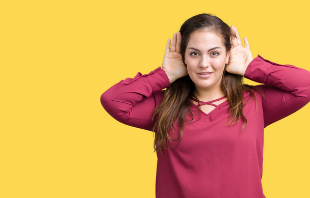 Όμορφη συν μέγεθος νεαρή γυναίκα απομονωμένη φόντο προσπαθεί να ακούω και τα δύο χέρια στο αυτί χειρονομία, περίεργος για κουτσομπολιό. Πρόβλημα ακοής, κουφός - Φωτογραφία, εικόνα