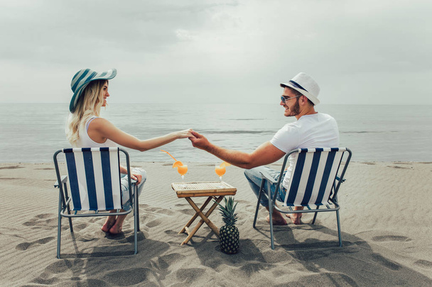 Couple on a deck chair relaxing on the beach. Happy couple enjoy on the beach during summer vacations - Фото, изображение