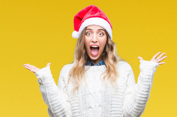 Üzerinde Noel şapka giyen güzel genç sarışın kadın deli kutluyor arka plan izole ve başarı için kaldırdı kollarını açarak hayrete ve heyecanlı çığlık gözleri açık. Kazanan kavramı - Fotoğraf, Görsel