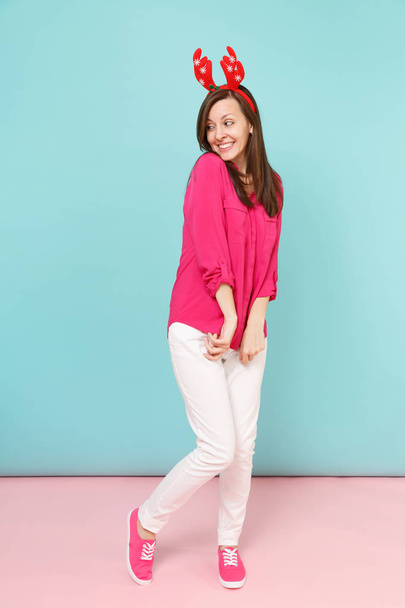 Ganzkörperporträt einer lustigen jungen Frau in rosa Hemdbluse, weißer Hose, Hirschhörnern, die isoliert auf hellrosa blauem Pastellhintergrund im Studio posiert. Mode-Lifestyle-Konzept. Attrappe Kopierraum - Foto, Bild