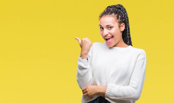 Young braided hair african american girl wearing winter sweater over isolated background smiling with happy face looking and pointing to the side with thumb up. - Foto, Imagen