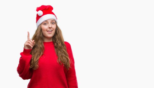 Nuori blondi nainen yllään joulupukki hattu yllättynyt idea tai kysymys sormella onnellinen kasvot, numero yksi
 - Valokuva, kuva
