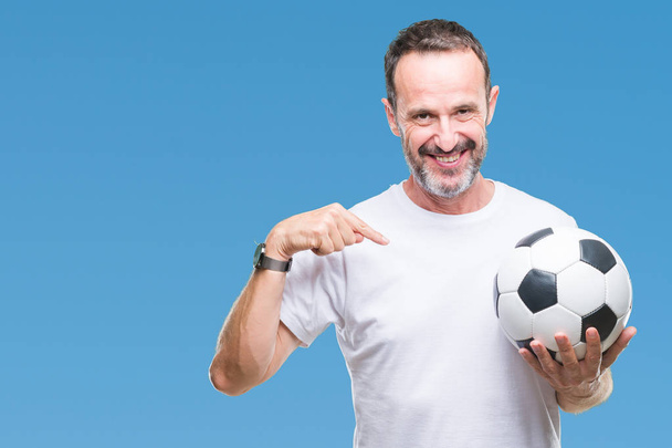 Middle age hoary senior man holding soccer football ball over isolated background with surprise face pointing finger to himself - Valokuva, kuva