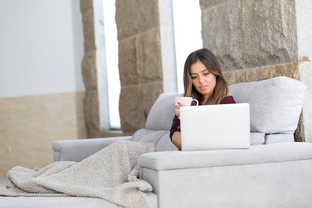 Mooie jonge vrouw thuis ontspannen op haar laptopcomputer - Foto, afbeelding