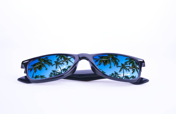 Солнечные очки в черной рамке с пальмами в отражении объективов на белом фоне, изолированные
. - Фото, изображение