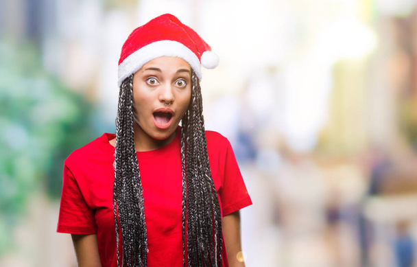 Joven trenzado pelo afroamericano chica con sombrero de Navidad sobre fondo aislado miedo y conmocionado con la expresión sorpresa, el miedo y la cara emocionada
. - Foto, Imagen