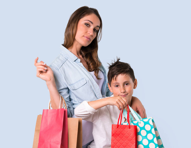 Matka a dcera drží mnoho nákupních tašek na modrém podkladu - Fotografie, Obrázek