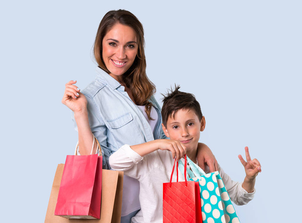 Mother and daughter holding a lot of shopping bags on blue background - Фото, зображення