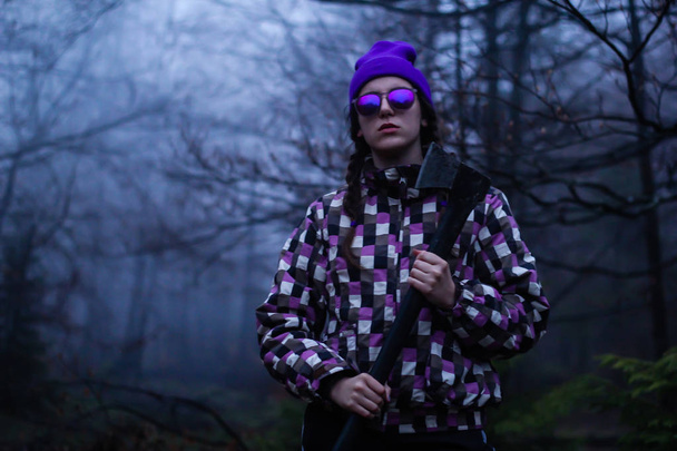 Morena con sombrero violeta, gafas y hacha. Retratos en el bosque. Fotografía de montaña en una chaqueta de esquí. Fondo oscuro. Montañas Cárpatas Ucranianas. Viajero
 - Foto, Imagen
