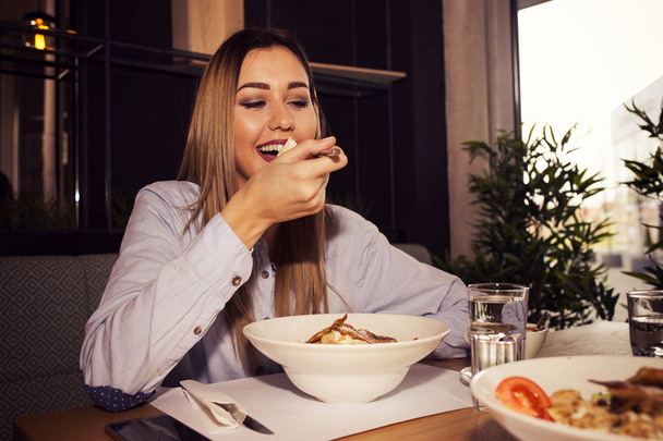 Young woman eating tasty food in a restaurant, having her lunch break. Close up - Zdjęcie, obraz