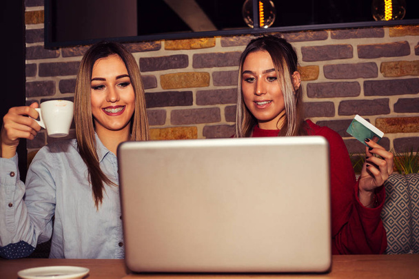 Kaksi onnellista ystävää ostaa verkossa kannettavan tietokoneen ja luottokortin kahvilassa
 - Valokuva, kuva