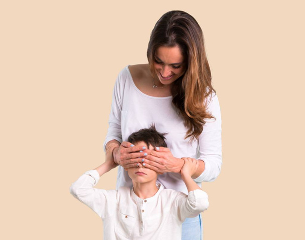 Mother and son covering eyes by hands on ocher background - Photo, Image