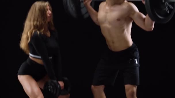Atlético hombre y mujer agacharse con peso extra, el entrenamiento de sus piernas y nalgas sobre un fondo negro en el estudio
 - Metraje, vídeo