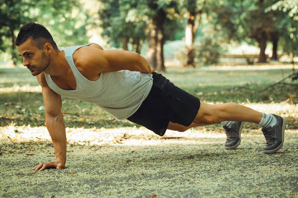 Portrait of a fitness man doing push ups in the park - Foto, Imagen