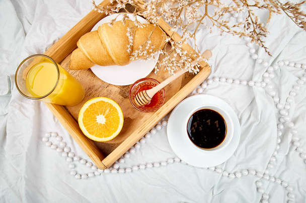 Guten Morgen. kontinentales Frühstück auf weißen Bettwäsche. Kaffee, Orangensaft, Croissants, Marmelade auf Holztablett von oben. Ansicht von oben. flach lag. Kopierraum. Hotelzimmer am frühen Morgen  - Foto, Bild