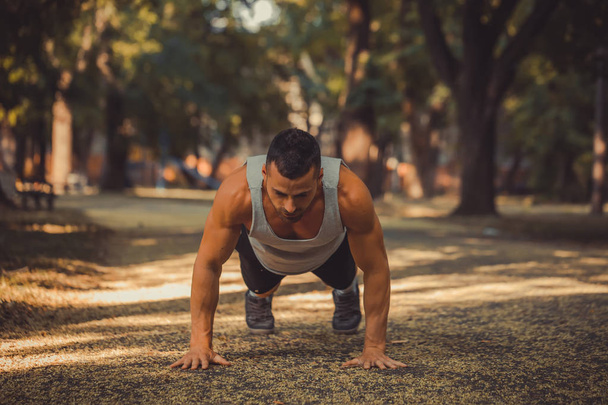 Push ups. Young muscular sportsman doing fitness exercise outdoors. Sport, fitness, workout concept - Photo, Image