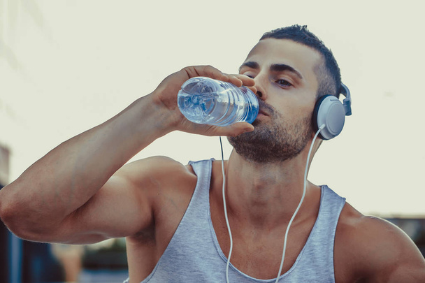 座っていると、トレーニング後の休息中にボトルから水を飲む若い男の肖像. - 写真・画像