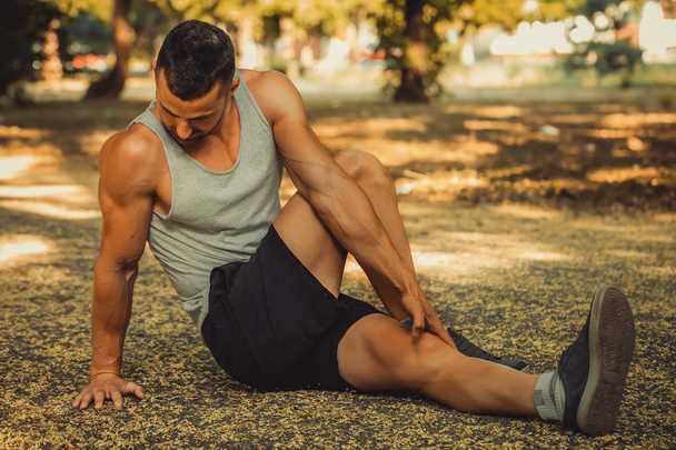 Jonge sportman doet stretching oefening, bereidt zich voor op ochtendtraining in het park. Fitness, sport, lifestyle concept - Foto, afbeelding