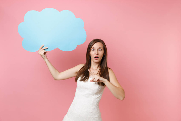 Shocked bride woman in wedding dress pointing index finger on blue empty blank Say cloud speech bubble isolated on pastel pink background. Wedding celebration concept. Copy space for advertisement - Photo, image