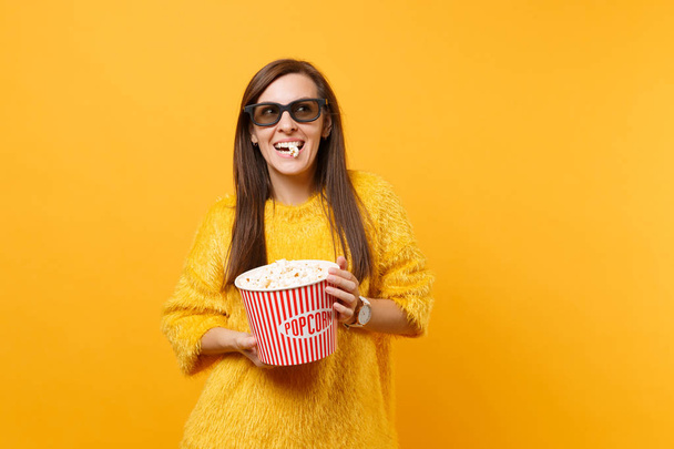 Πορτρέτο της χαρούμενη happy νεαρό κορίτσι σε γυαλιά imax 3d βλέποντας ταινία ταινία και τρώγοντας ποπ κορν από κουβά που απομονώνονται σε φωτεινό κίτρινο φόντο. Άνθρωποι ειλικρινή συναισθήματα στον κινηματογράφο, αντίληψη του τρόπου ζωής - Φωτογραφία, εικόνα