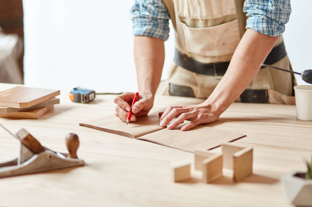 Closeup view of a carpenter using a red pencil to draw a line on a blueprint - Foto, Imagem