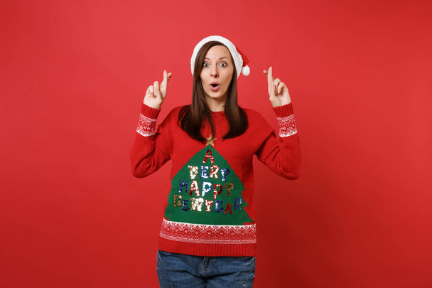 Amazed Santa girl keeping fingers crossed, mouth open, looking surprised, wait for special moment isolated on red background. Happy New Year 2019 celebration holiday party concept. Mock up copy space - Valokuva, kuva
