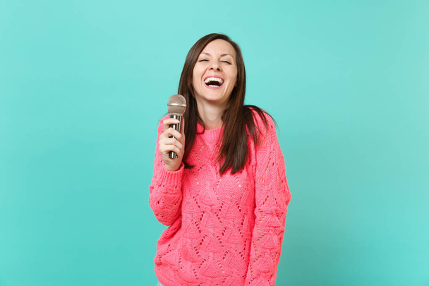Nevetve vicces fiatal nő kötött rózsaszín pulóver tartja a kezében, énekelni a dalt elszigetelt kék türkiz háttér, portré stúdió mikrofon. Emberek életmód fogalma. Mintája fel másol hely - Fotó, kép