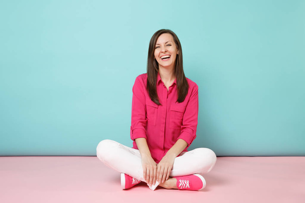 Full length portrait of smiling young woman in rose shirt blouse, white pants sitting on floor isolated on bright pink blue pastel wall background studio Fashion lifestyle concept. Mock up copy space - Fotografie, Obrázek