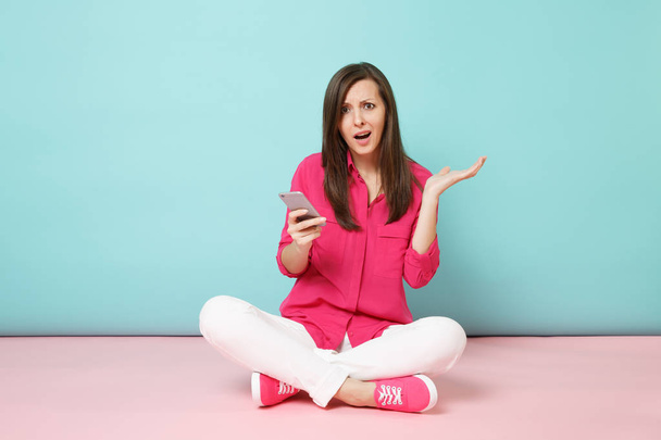 Full length portrait of young fun woman in rose shirt white pants sit on floor hold cellphone isolated on bright pink blue pastel wall background studio. Fashion lifestyle concept. Mock up copy space - Photo, Image