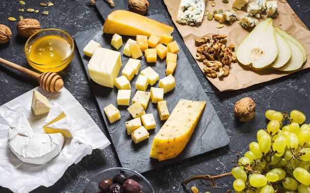 Diferentes tipos de quesos a bordo, olivos, frutas, almendras y copas de vino sobre mesa de piedra negra
 - Foto, imagen