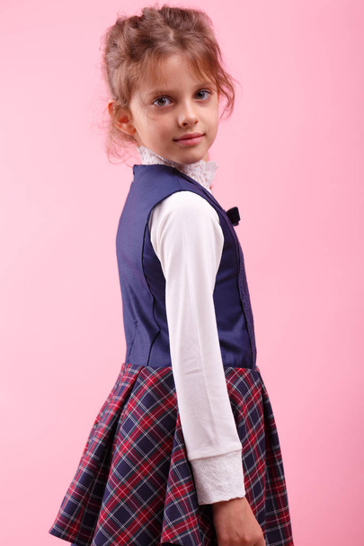 A cute little girl in a school uniform on a pink background. Education, school concept - Foto, Imagem