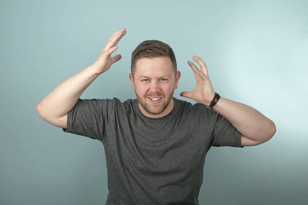 Hombre enojado frustrado gruñendo y haciendo gestos con sus manos a cada lado de su cabeza sobre un fondo gris
 - Foto, Imagen