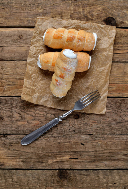 Vista desde arriba del tubo de crema de pastelería lleno de crema - pastel de postre - tradicional dulce checo en papel de hornear y tenedor en la mesa de madera
 - Foto, imagen
