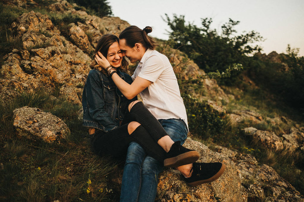 Młody mężczyzna całuje dziewczynę w policzek siedząc razem na zboczu skalistej góry - Zdjęcie, obraz