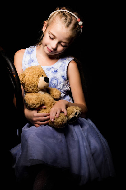 Little girl with a teddy bear on a black background. - Foto, Bild