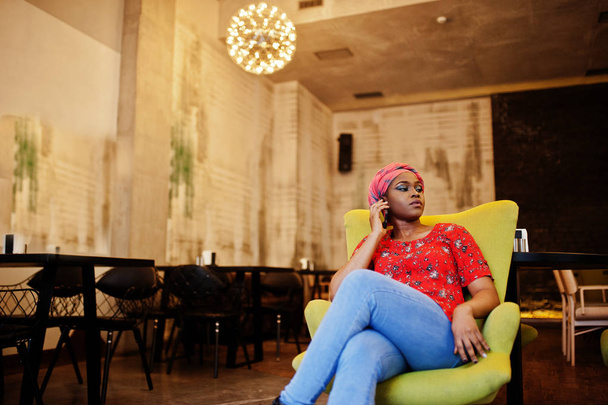 Stylish african woman in red shirt and hat posed indoor cafe and speaking mobile phone. - Zdjęcie, obraz