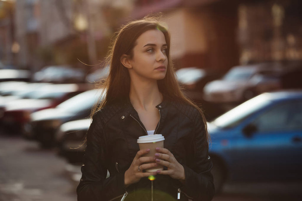 Beautiful woman holding paper coffee cup and enjoying a walk in the city - Фото, зображення
