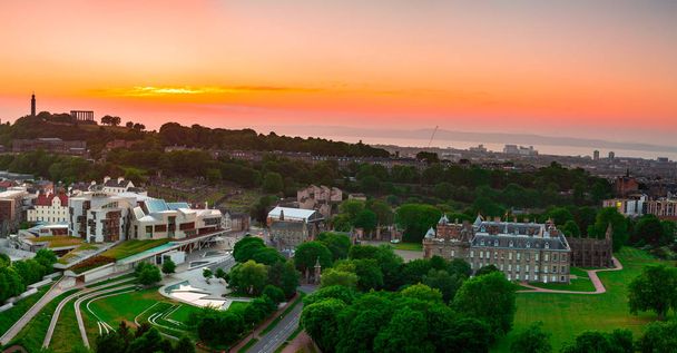 Переглянути більше палац Holyroodhouse, шотландський парламент і Калтон Хілл під помаранчевого заходу сонця небо в Единбурзі, Шотландія. - Фото, зображення