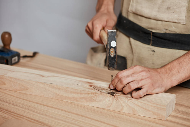 The carpenter hammering down a nail to wooden plank, making a furniture. - Foto, Imagen