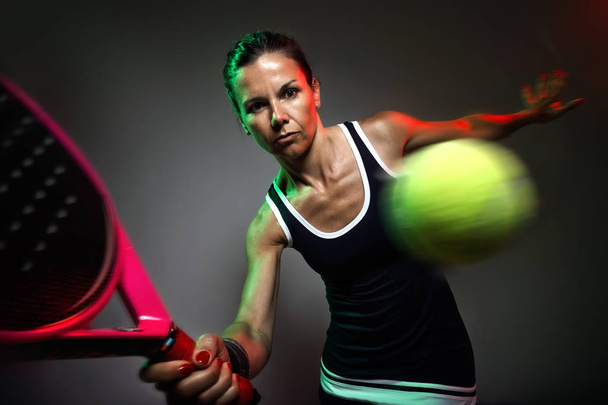 Portrait of adult fitness woman playing padel indoor. Isolated on black. - Foto, immagini