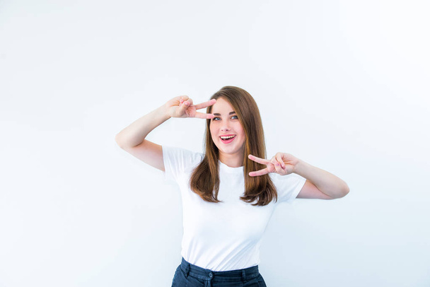 Portrait of happy girl flirting at camera and showing dancing gesture. Caucasian woman looking through fingers in victory sign isolated on white background. Positive emotion expression. Copy space - Foto, immagini