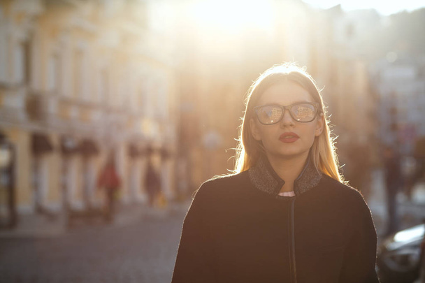 Outdoor portrait of stylish blonde woman with red lips wearing glasses coat, posing at the old sunny street. Space for text - Foto, Bild