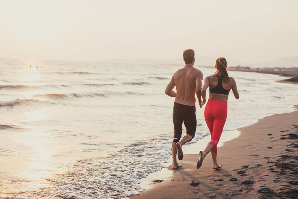 Handsome Caucasian man and beautiful woman running on sandy beach in sunset. - Фото, зображення