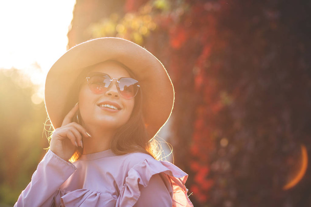 Aantrekkelijke lachende vrouw met natuurlijke make-up dragen van hoed en zonnebril, poseren in zonnig park. Ruimte voor tekst - Foto, afbeelding