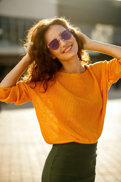 Молодая женщина в солнцезащитных очках в трико и прогуливается по солнечной улице
 - Фото, изображение
