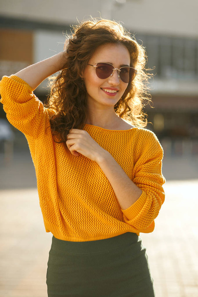 Αξιολάτρευτο νεαρό μοντέλο σε γυαλιά ηλίου που φοράει μοντέρνο ντύσιμο και το περπάτημα στο ηλιόλουστο δρόμο - Φωτογραφία, εικόνα