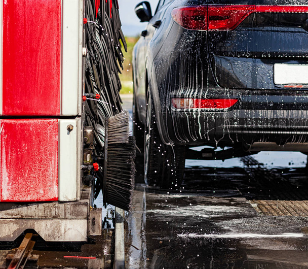 赤と黒のブラシを回転させる自動洗車で黒の車。アルミ ホイールの洗浄の詳細. - 写真・画像
